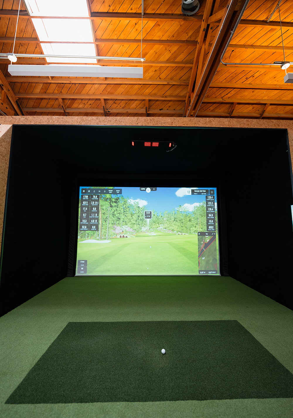 The interior of an indoor golf space, showing a golf ball and table with a golf simulator in the background